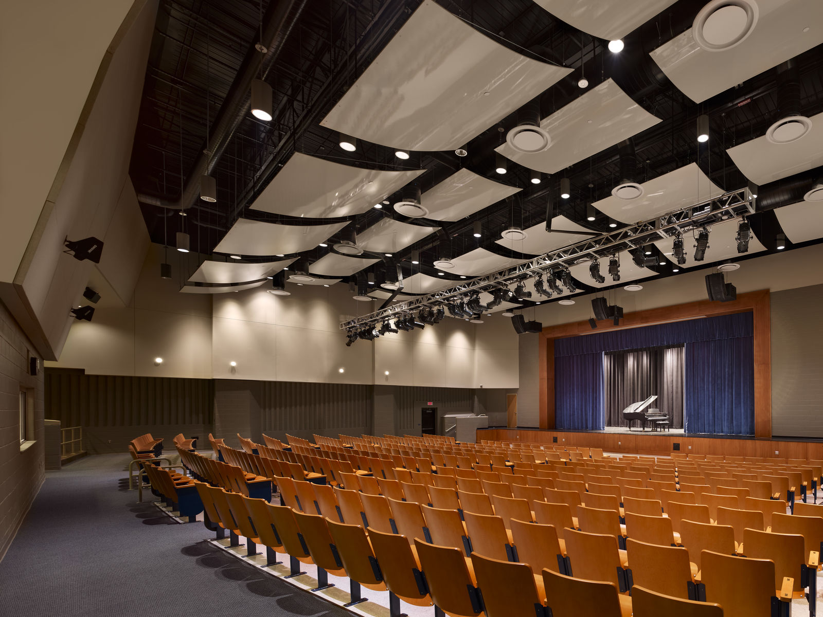 A modern auditorium in Philadelphia with rows of empty wooden seats faces a stage with a grand piano. Neutral walls and white acoustic panels blend civic elegance with historic preservation, while dark curtains and spotlights highlight the space.
