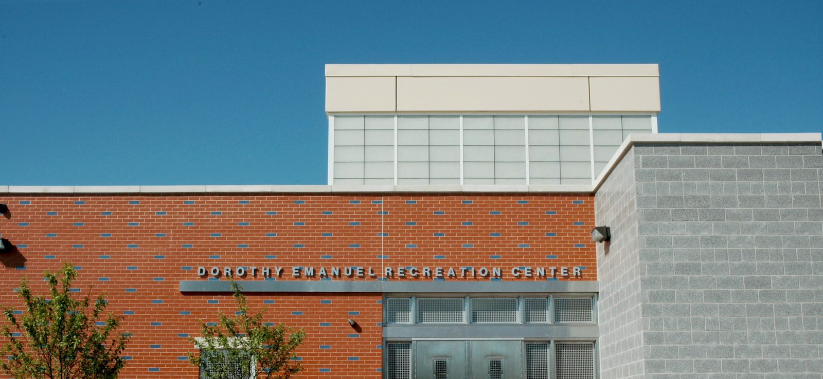 Front view of the Dorothy Emanuel Recreation Center in Philadelphia, a modern brick and concrete civic building under a clear blue sky. The building’s name is visible above the entrance.