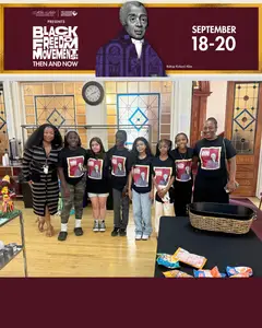 A group of people in matching shirts pose in front of stained glass windows at an indoor event called Black Freedom Movements: Then and Now, held September 18-20. Snacks are on a table in the foreground.